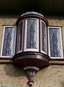 Ornate bay window with diamond-patterned glass and red trim on a textured wall.